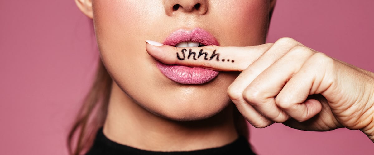 Woman holding her finger between her lips and the sound "shhh" is written on her finger. Highlighting that in our office lip filler is done so naturally it can be our secret.