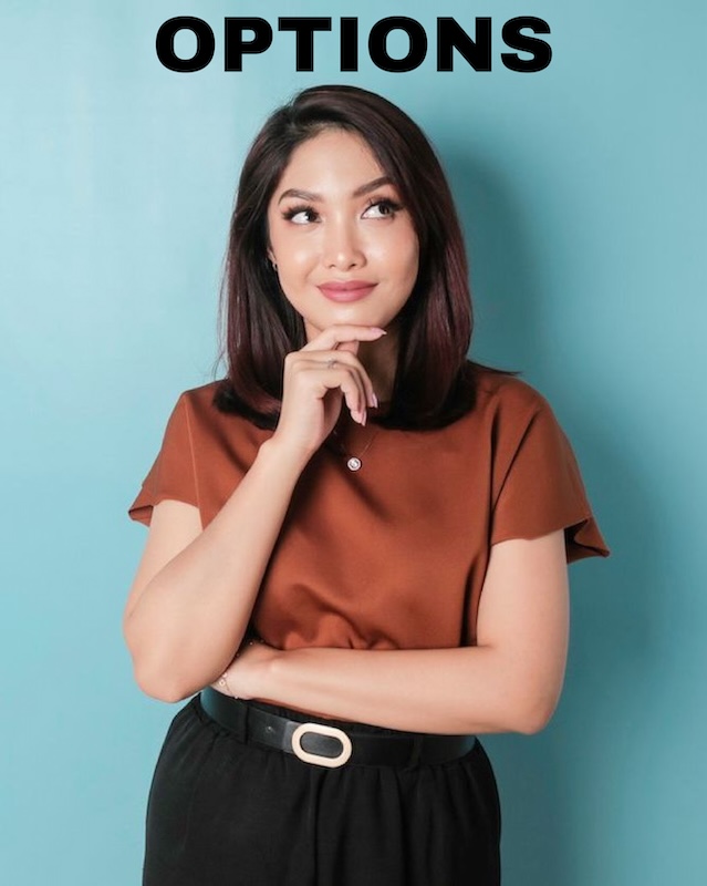 A woman standing with one hand supporting chin wondering about options for labia puff surgery,